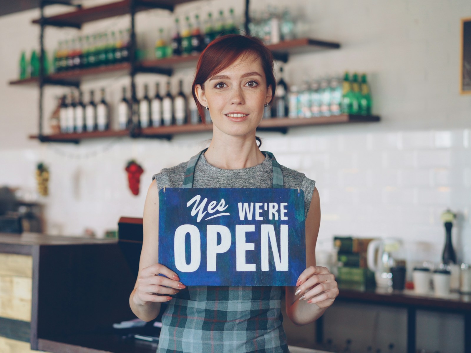 A smiling cafe owner holding a “Yes, we're open” sign